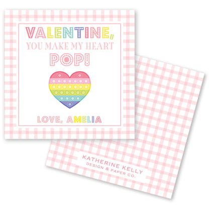 The image is a Valentine's Day card with a pink and white checkered background. The card features a heart-shaped pop-up design and text that reads "Valentine! You make my heart pop!" The card also includes the name "Love, Amelia" and the logo of "Katherine Kelly Design & Paper Co."