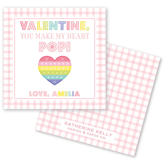 The image is a Valentine's Day card with a pink and white checkered background. The card features a heart-shaped pop-up design and text that reads "Valentine! You make my heart pop!" The card also includes the name "Love, Amelia" and the logo of "Katherine Kelly Design & Paper Co."