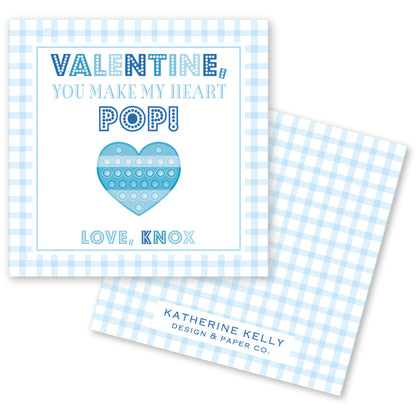 The image is a Valentine's Day card with a blue and white checkered background. The card features a heart-shaped pop-up toy and a message that reads "Valentine! You make my heart POP!" The card also includes the text "Love, Knox" and "Katherine Kelly Design & Paper Co."